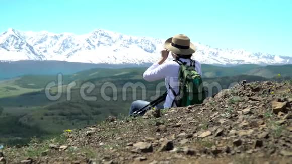 那个带着绿色背包的旅行者的女人坐着看雪山鹰在天空中飞翔视频的预览图