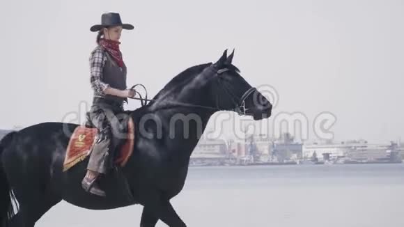 骑马小牛仔骑着黑马在河滩4k视频的预览图