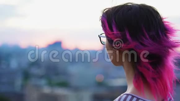 年轻女孩在城市背景下享受日落粉红色的头发和眼镜视频的预览图