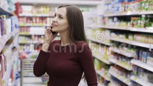 漂亮的黑发女人在电话里聊天在超市里选东西视频的预览图