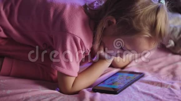 一个学龄前的小女孩金发穿着一件粉红色的T恤和一条浅色裤子躺在床上视频的预览图