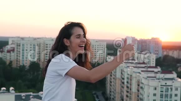 女孩在一栋高层建筑屋顶上的智能手机上拍照视频的预览图