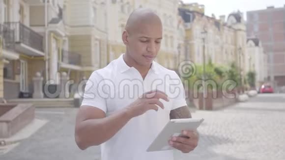 一幅英俊自信秃顶的中东男子在平板电脑上打字的肖像站在老街前视频的预览图