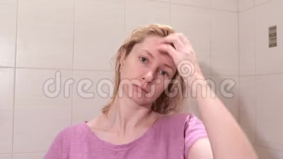 中年金发女人在浴室用梳子刷湿头发视频的预览图