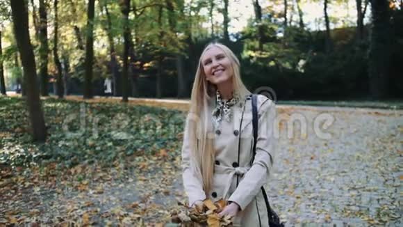 小女孩走在秋天的公园里把金色的叶子抛在空中慢动作视频的预览图