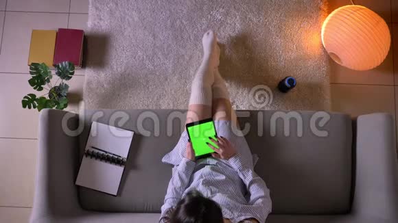 年轻迷人的女性在平板电脑上打字的特写镜头绿色的彩色屏幕坐在可爱的沙发上视频的预览图