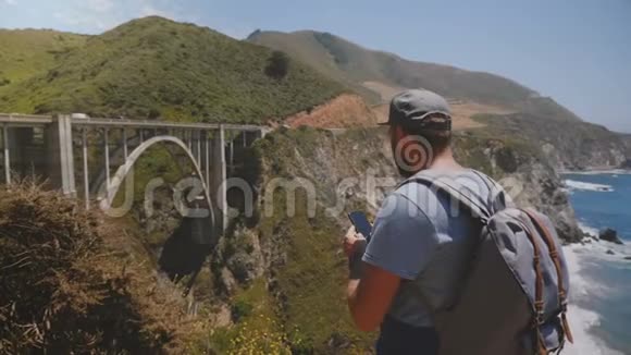 快乐中年博主游客带背包拍摄标志性的比克斯比溪桥美国全景智能手机视频视频的预览图