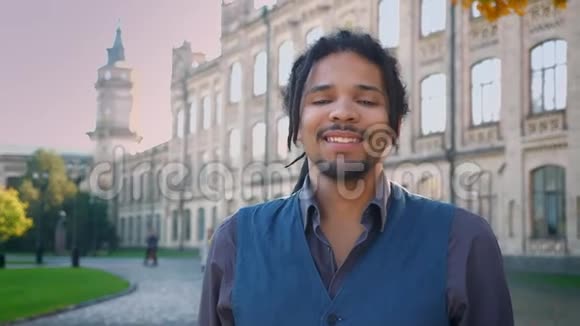 有魅力的非裔美国人的肖像在大学背景下带着可怕的微笑进入镜头视频的预览图