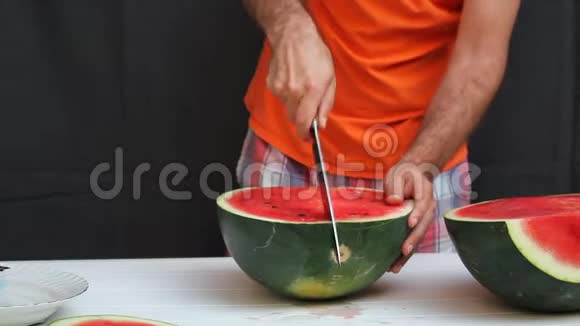 穿着橙色衬衫的人正在用厨师刀切西瓜黑色背景视频的预览图
