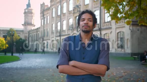 非裔美国人带着双臂的肖像在大学背景下严肃地凝视着镜头视频的预览图