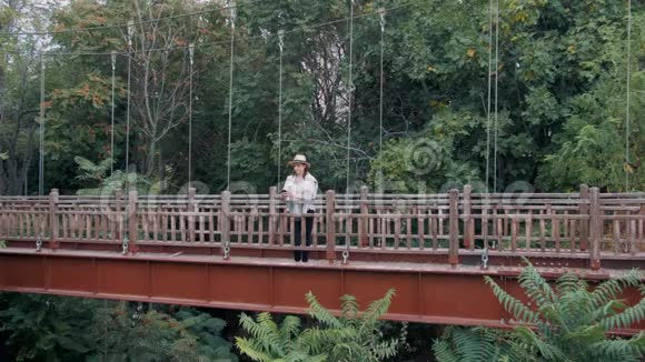千禧年嬉皮士女游客使用智能手机在桥上的丛林视频的预览图
