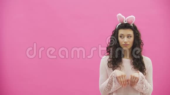 年轻漂亮的夫妇站在粉红色的背景上在这期间他们做兔子的动作女人把她视频的预览图