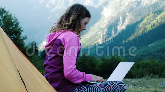 旅游妇女使用笔记本电脑的本质自由职业者打字在帐篷附近的背景下旅行视频的预览图