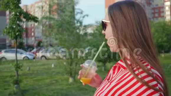 女人从稻草中喝橙汁在城市里散步近距离射击视频的预览图