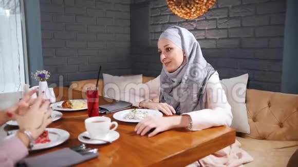 一位穆斯林妇女坐在餐桌旁的咖啡馆里喝着果汁说话视频的预览图