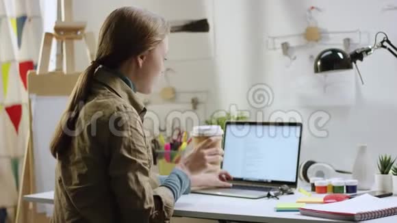女人一边喝咖啡一边在笔记本电脑上发短信视频的预览图