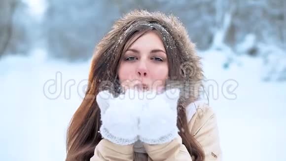 戴着白色围巾的小女孩走在森林里对着镜头吹着一把雪视频的预览图