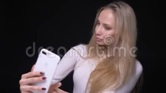 年轻漂亮的金发女性在手机上自拍的特写照片脸上带着微笑背景与黑色隔离视频的预览图