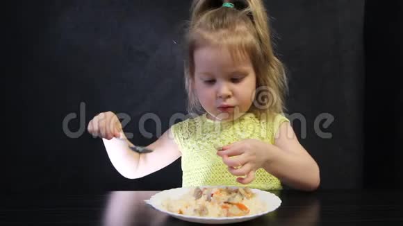 孩子们在黑桌上用勺子在黑色背景上吃煮熟的米饭和蘑菇视频的预览图