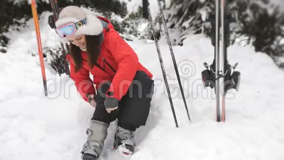 准备滑雪的年轻女子她穿上鞋子坐在滑雪场的雪地里视频的预览图