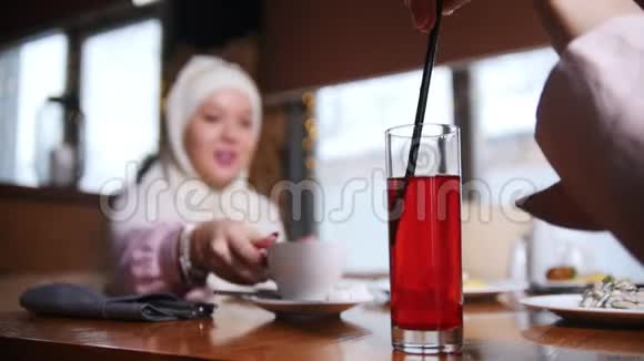 一位年轻的穆斯林妇女坐在现代咖啡馆里交谈一个女人用吸管搅拌饮料视频的预览图