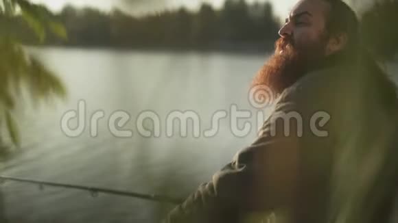 长胡子的渔夫坐在河岸上钓鱼费舍尔挥动着他的朋友的手河流视频的预览图