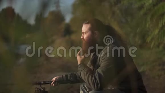 长胡子的渔夫在河岸上钓鱼费舍尔抚摸他的胡子河流捕鱼视频的预览图
