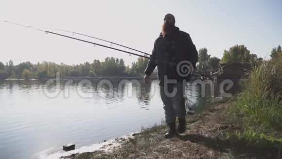 长胡子的成年渔夫带着鱼竿和鱼网在河边散步那个人望向远处视频的预览图