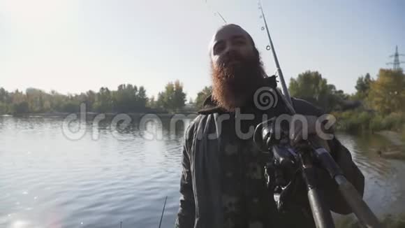 快乐微笑的渔夫长着胡子带着钓鱼竿在河岸上散步慢动作视频的预览图