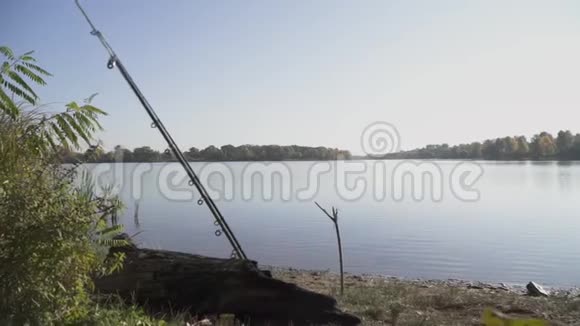 两根钓鱼竿躺在河岸上背景是平静的水绿树和干净的蓝天视频的预览图