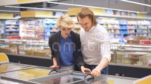 快乐的白种人夫妇从超市冰箱里选择冷冻食品视频的预览图