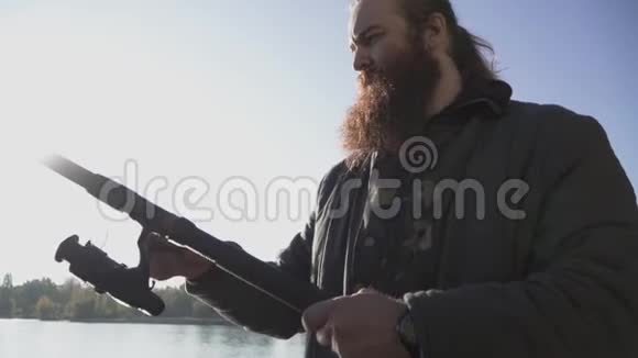 渔夫旋转钓鱼卷轴长胡子的人拿着钓鱼竿在河上河流捕鱼慢动作视频的预览图