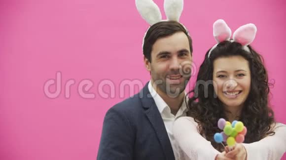 粉色背景的年轻创意情侣头上长着黑耳朵在此期间妻子手持装饰物视频的预览图