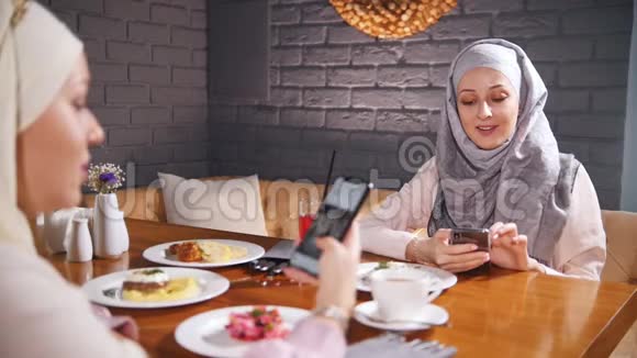 两个穆斯林妇女坐在餐厅的一张桌子上坐在电话里展示图片视频的预览图