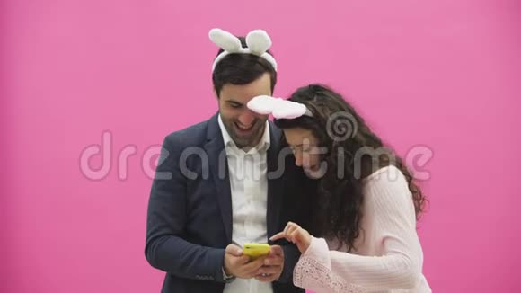 年轻情侣的粉色背景头上有贪婪的耳朵在这张复活节照片中赛菲打电话视频的预览图