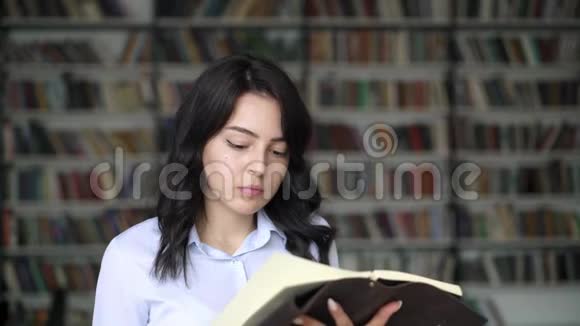 在图书馆书架背景上翻书的年轻女子视频的预览图