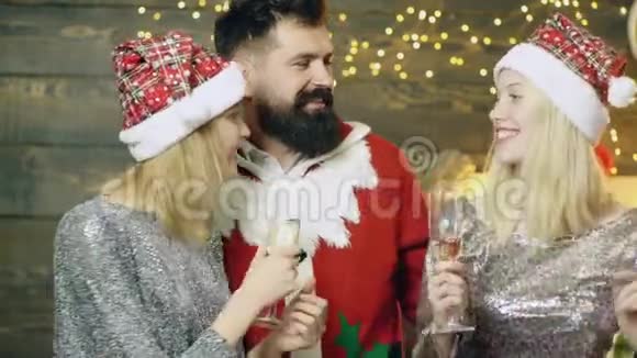 穿着桑塔服装的大胡子男人和戴着新年帽子的两个女孩在圣诞节喝香槟玩得开心新年视频的预览图