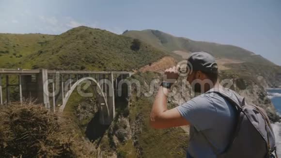 年轻快乐兴奋的旅游男子背着背包观看比克斯比峡谷大桥的史诗般美丽的风景走开了视频的预览图