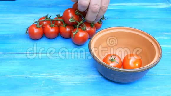 人类的双手从一张蓝色的木桌上的树枝上摘出樱桃番茄然后把它们放进一个陶瓷碗里视频的预览图