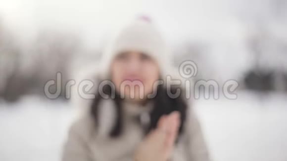 特写深色头发的年轻女性肖像粉红色的嘴唇米色的羽绒服和帽子擦手寒冷中的霜冻视频的预览图