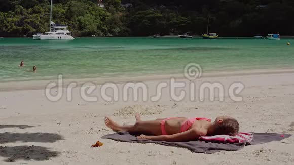 美丽的年轻女孩躺在沙滩上晒太阳在一个夏天阳光明媚的日子视频的预览图