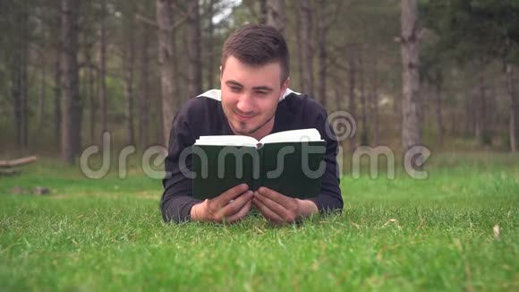 一个年轻人躺在森林里的绿草上看书休息放松愉悦视频的预览图