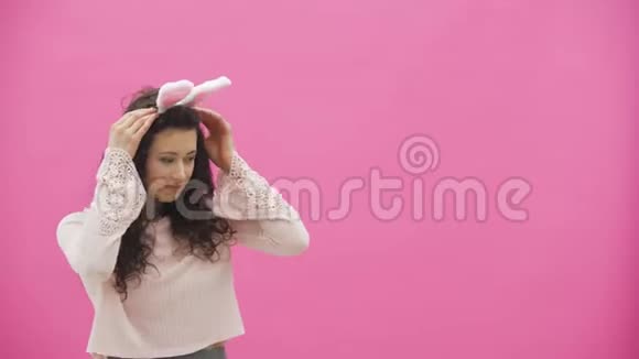 年轻漂亮的女孩站在粉红色的背景上女孩像兔子一样移动轻轻的看着镜头笑了视频的预览图