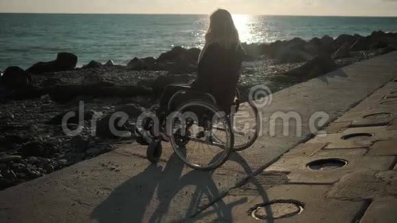 一位患有脊椎病的年轻女士坐在海边的轮椅上视频的预览图