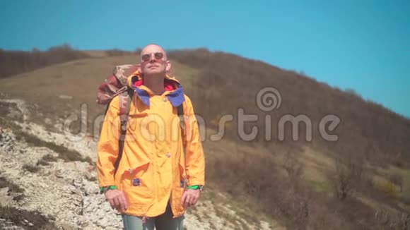 一个穿着黄色夹克眼镜和一个大型旅游背包的人站在山上欣赏着风景视频的预览图