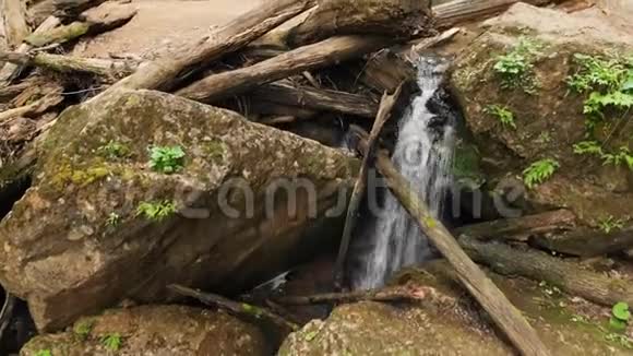 夏季森林中的大石头和干燥的老原木之间的小瀑布的近距离鸟瞰森林凉爽视频的预览图