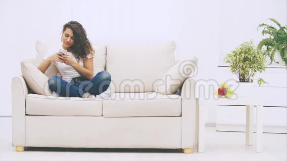 可爱的古怪的非裔美国女孩正坐在沙发上的洛托斯的位置手里拿着电话发着短信视频的预览图