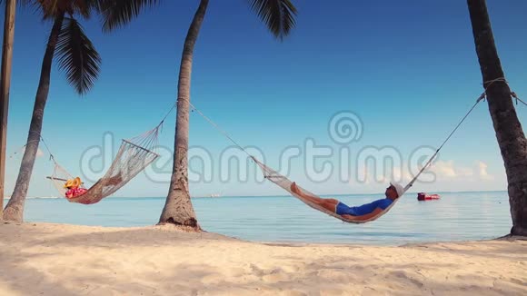 男人和女人在热带岛屿海滩的吊床上放松视频的预览图