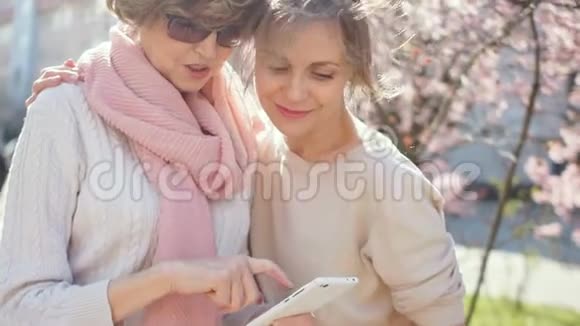 女儿和母亲通过智能手机上的照片春天阳光明媚的街道上的肖像母亲节视频的预览图