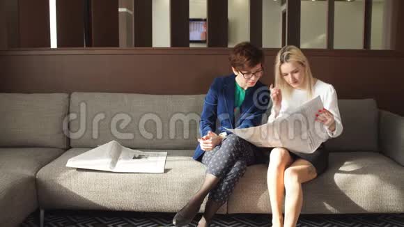 两个女朋友坐在沙发上看报纸新闻视频的预览图